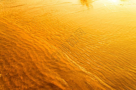 金色光从海面的水浪和日落的沙背景图片