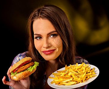 女人吃炸薯条和汉堡包学生在桌子上吃快餐在深色背景上宣传快餐因为不愿意做饭背景图片