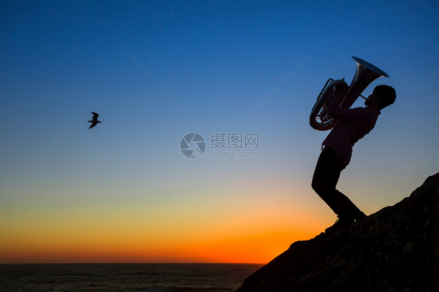 令人惊异的日落时音乐家在海边吹奏图片