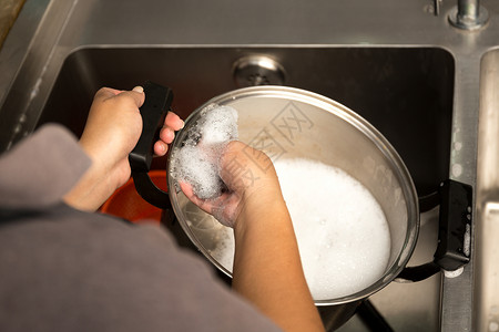 妇女用手洗不锈钢锅在厨房水槽中用图片