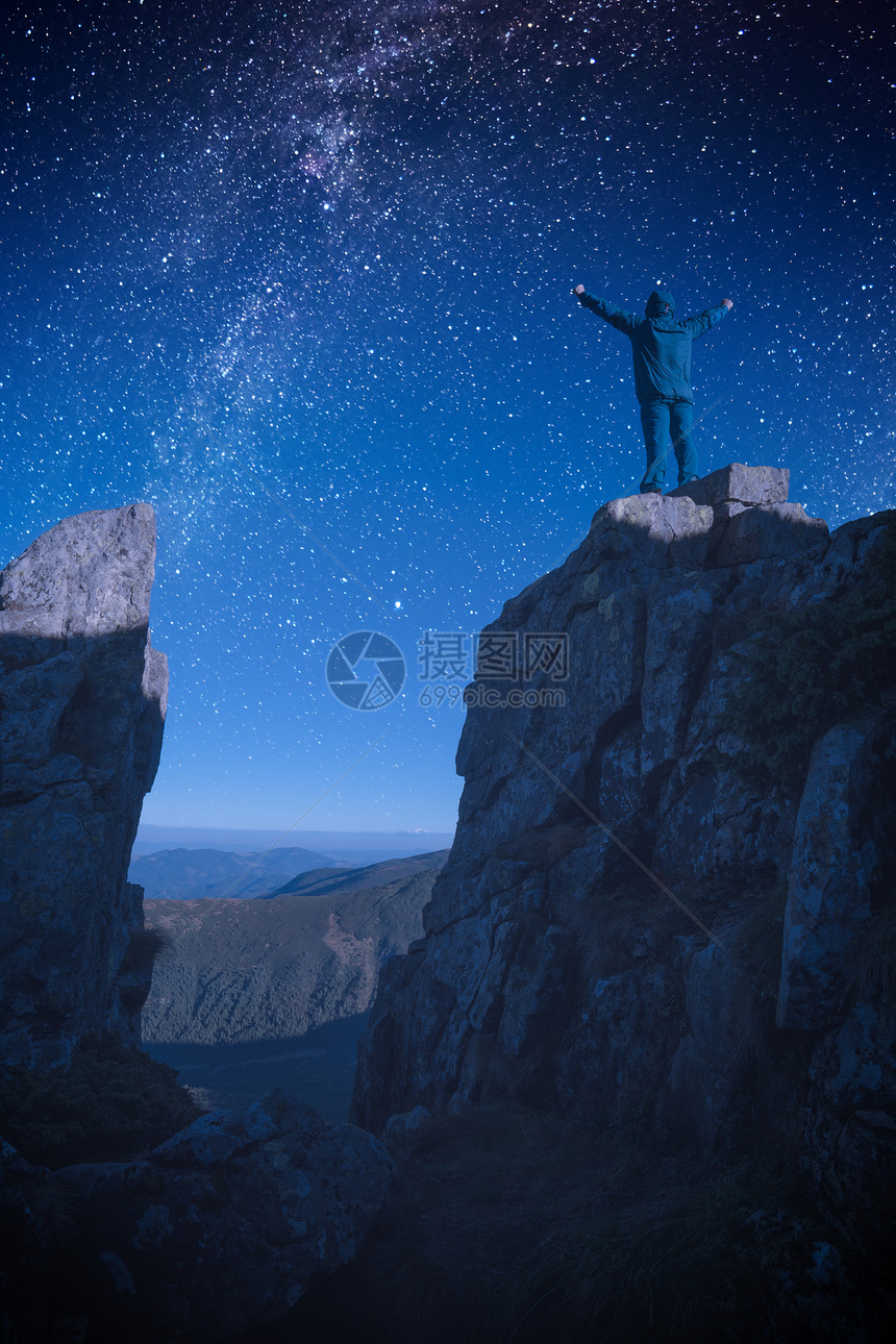 站在岩石悬崖边缘的人手举起来与夜景对峙在星般的天空中图片