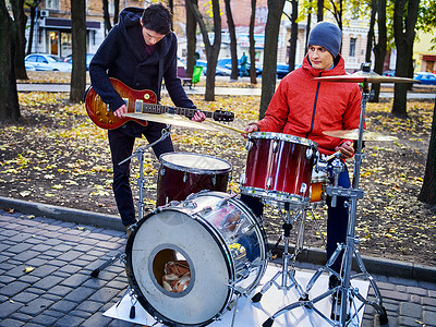 节日音乐队男音乐家在城市公园演奏震荡乐器的棍棒鼓和吉他特写图片