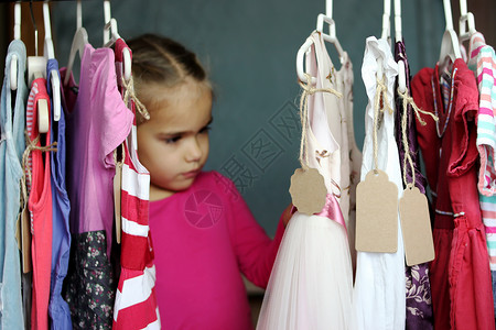 可爱的学龄前女孩在儿童时装店的许多衣服中选择一件新衣服图片