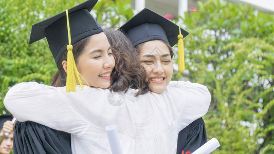 两个亚洲女学生穿着毕业礼服戴着帽子拥抱父母在祝贺图片