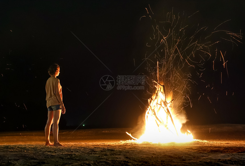 年轻女旅行者在夜间感受海滩篝火的热度和火花图片