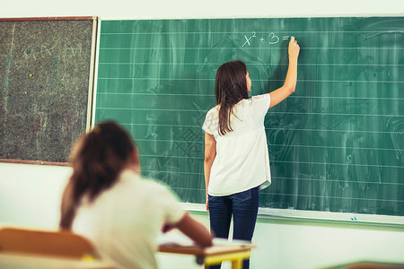 聪明可爱的女学生用粉笔在黑板上写字图片
