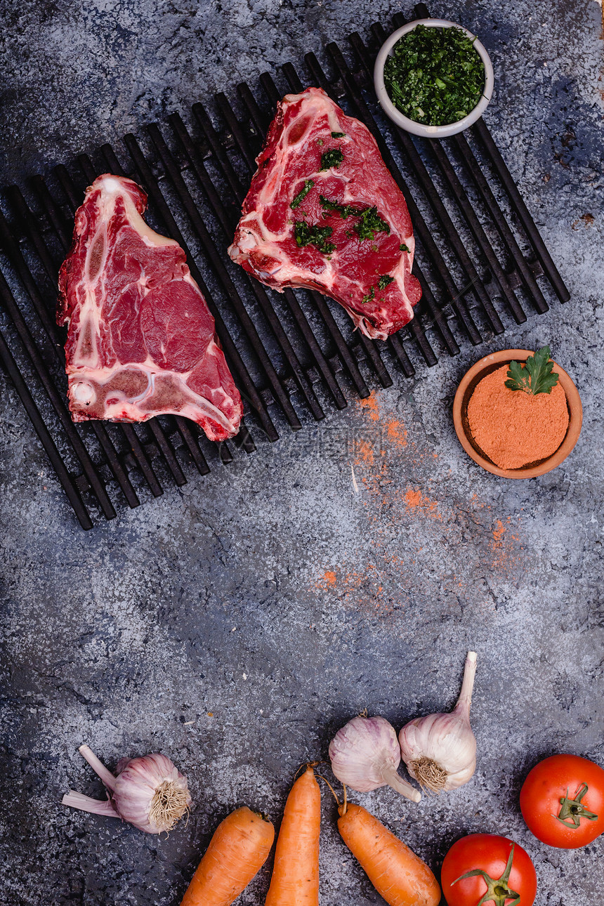 混凝土桌上加香料和蔬菜的生肉的顶部视图图片