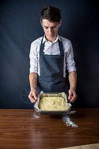 穿制服黑围裙做蛋糕的年轻男厨师图片