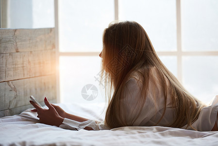 女孩在床上拿着电话年轻女人有背景图片