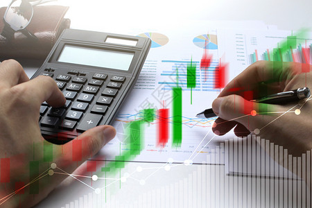 双重曝光业务手用计算器和笔与股票市场或金融图表的金融投图片
