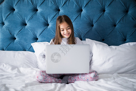 小女孩躺在床上在卧室里玩笔记本电脑她图片