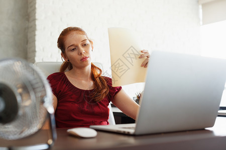 夏天热浪期间在办公室使用电脑笔记本电脑工作的年轻红发女人的画像背景图片
