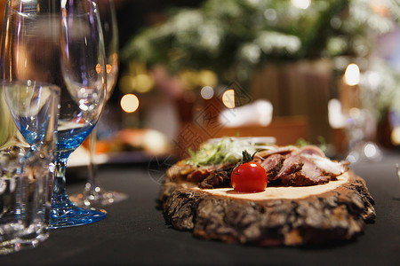 切片自制肉品腌肉培根新鲜西红柿木块上的黄瓜餐桌上的酒杯和黑色桌布图片