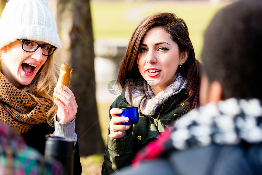 年轻女朋友在冬日户外喝热饮料时聊图片