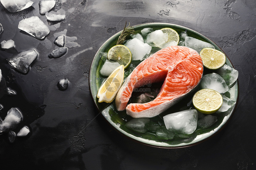 深底黑面圆盘上带冰和柠檬切片的新鲜鲑鱼图片