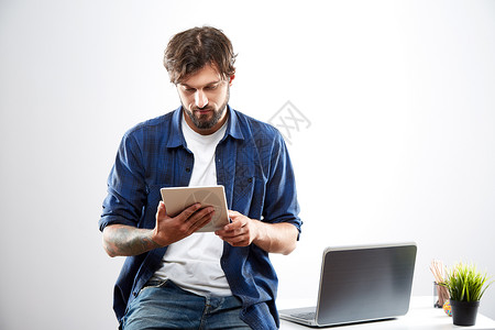 年轻人穿着蓝色衬衫坐在笔记本电脑旁图片