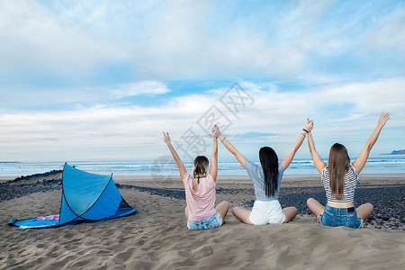 三名年轻女背影是举起手来在海岸线背景图片