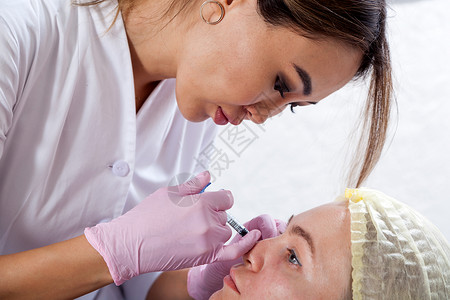 一位黑发女亚洲美容师的特写镜头将肉毒杆菌注射液注射到一位年轻女颧骨图片