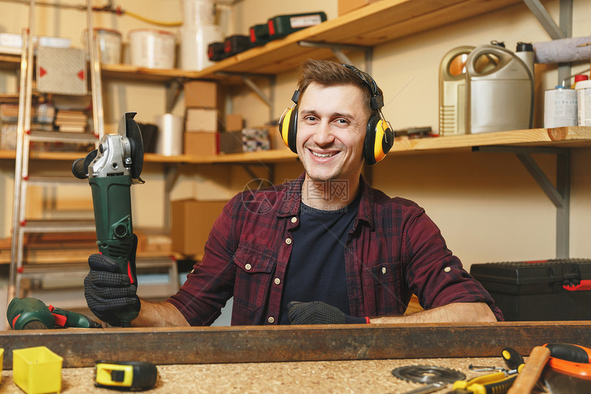 身穿格子衬衫黑色T恤在木工车间用不同工具作的隔音耳机用电锯铁的帅气微笑的图片