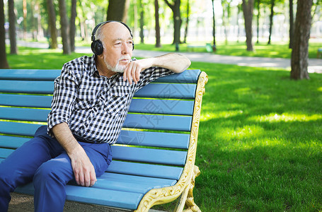 体贴的老人在户外听音乐戴耳机的老人坐在公园的长椅图片
