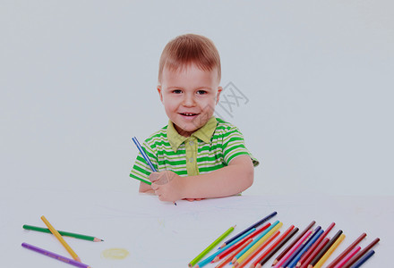 鼓动坐在桌边的小男孩用蜡笔画在图片