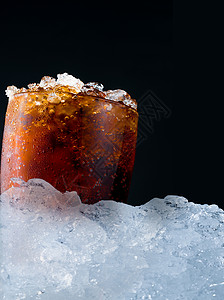 玻璃杯中碎冰块的软饮料放在深色背景上的一堆冰块上图片