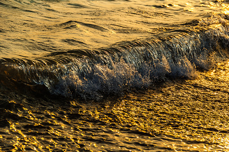 海浪水泡沫在日落时流图片