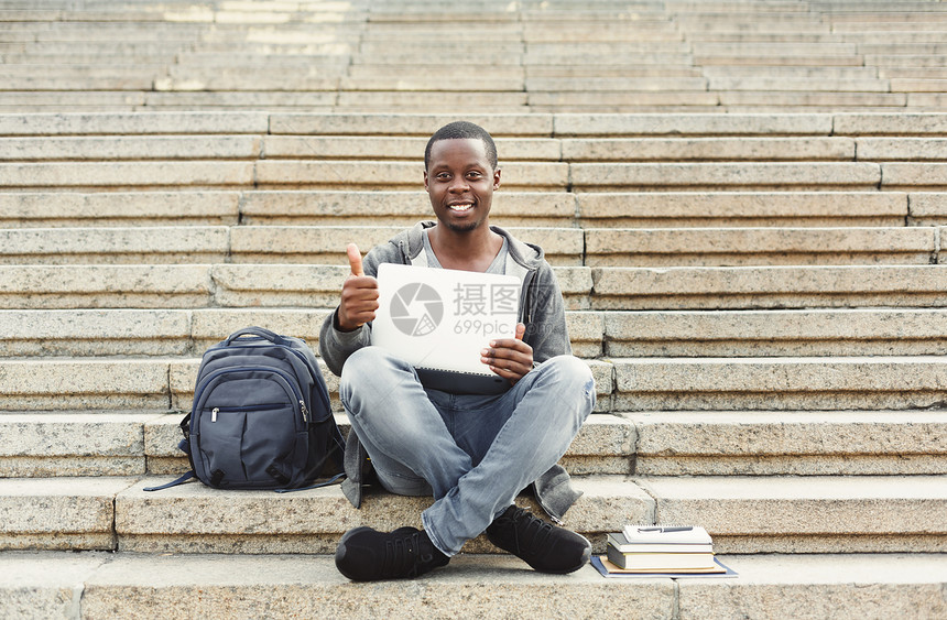 微笑坐在楼梯上举起拇指用笔记本电脑工作准备大学校园考试的非洲美籍学生图片