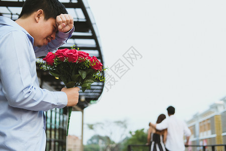 亚洲伤心欲绝的男人拿着一束红玫瑰在看到女人和另一个男人约会时感到悲伤心碎背景图片