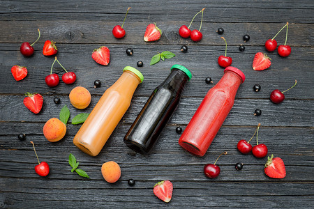 黑色木质背景上的三瓶果汁和水果食物概念图片