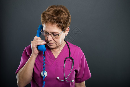 高级女医生在黑色背景的蓝色大电话听筒上交谈的肖像图片