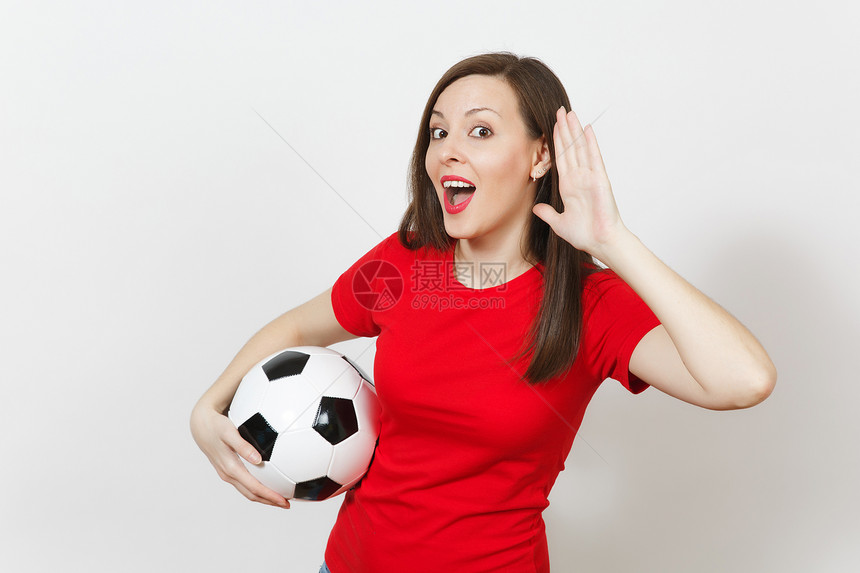 美丽的欧洲年轻女子足球迷或穿着红色制服窃听的球员听力手势拿着白色背景上孤立的足球体育踢足球健康健康的图片