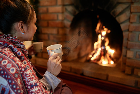 年轻女子喝茶看家里壁炉的火光背景图片