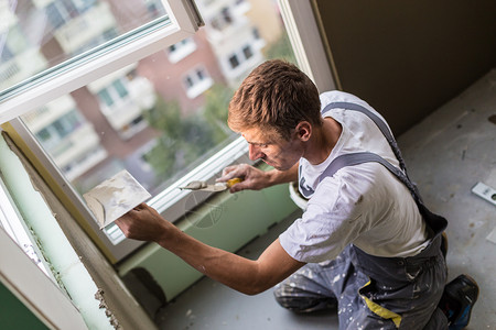 三十岁的体力工人用抹墙工具装修房子泥水匠用浮子和石膏翻新室内图片