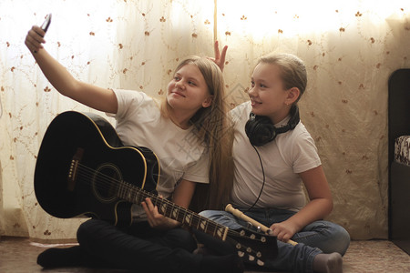 两名女青少年在家中自拍和摆姿势的乐器坐在地板上图片