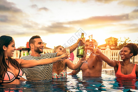 一群快乐的朋友在日落时用香槟欢呼庆祝泳池派对年轻人在豪华热带度假胜地笑着用起泡酒敬青年背景图片
