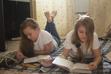 两个十几岁的女孩在看书和画时躺在家里的地板图片