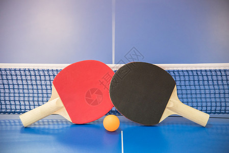 乒乓球的橙色球和两个红色和黑色的木制球拍图片