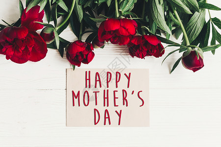 母亲节快乐的文字标志在工艺纸卡上美丽的红牡丹在白色木质朴的背景上图片