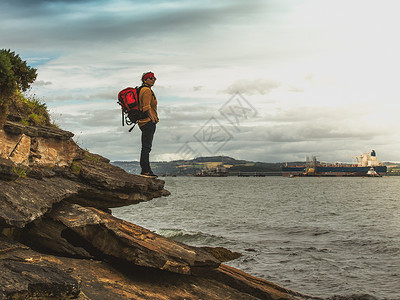 一个带着背包的旅游妇女站在岩石上看着船图片