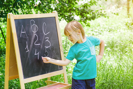 可爱的小男孩在花园的黑板上写信和数字图片