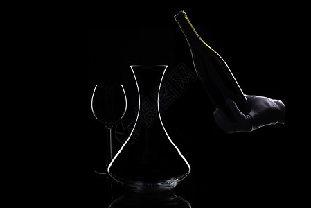 酒杯瓶子和醒酒器的剪影在孤立的黑色戴白手套的手在底部和醒酒器中背景图片