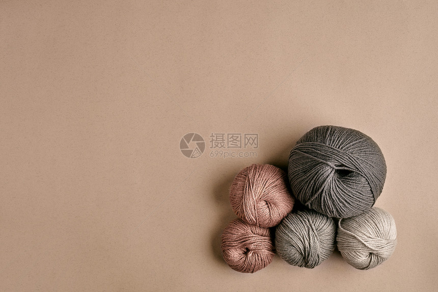 米色背景上的灰色和棕色针织羊毛和织针织作为一种针线活五颜六色的毛线球和织针顶视图静物复图片