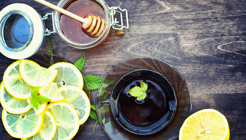 蜂蜜和柠檬木桌上的蜂蜜棒和柠檬片杯子里的茶和罐子里图片