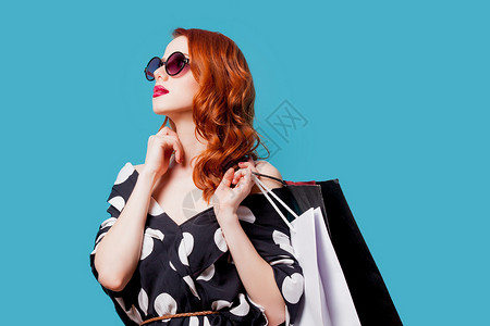 戴着太阳镜的红发女人蓝色背景的购物袋图片