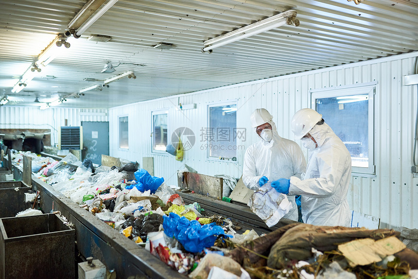 两名身穿生物危害套装的工人在垃圾加工厂作的画像图片