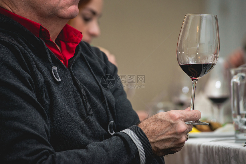 男人拿着一杯红酒品酒时桌上有很多不同的酒杯人们会考虑葡萄酒的颜色并尝试在不同的玻璃杯中图片