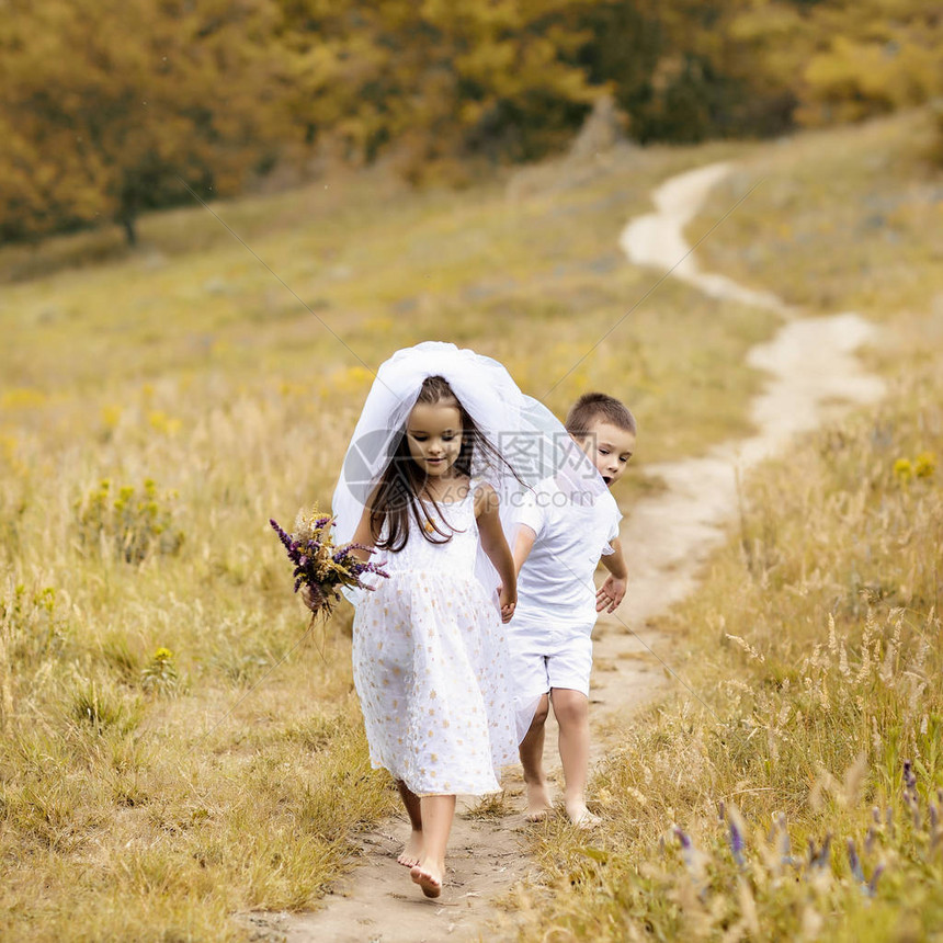 年轻的新娘和新郎在户外玩婚礼夏天孩子们喜欢新婚夫妇新娘白色礼服和新娘面纱的小女孩和她的小男孩新郎一起散步图片