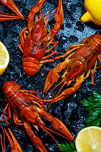 新鲜煮熟的龙虾有柠檬和绿鱼在黑图片