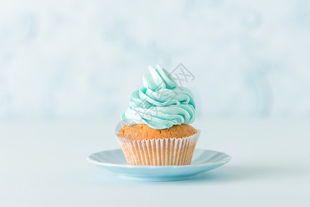 盘子上有蓝色奶油装饰的纸杯蛋糕蓝色柔和的水平横幅图片